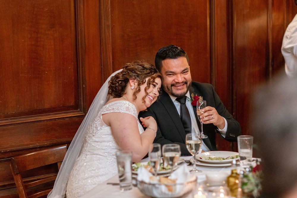 Newlyweds share emotional moment at reception dinner table surrounded by decorative elements.