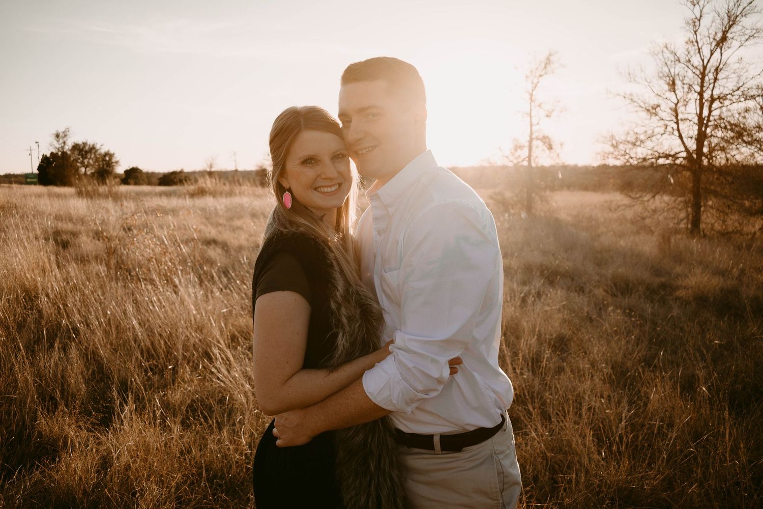 Intimate engagement portrait of couple holding each other in sunlit prairie field.