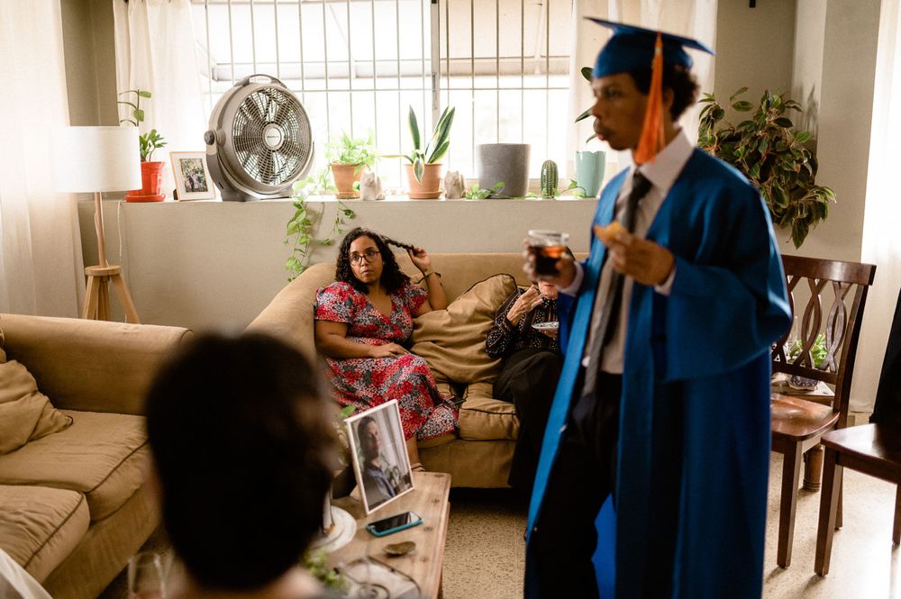 Graduation celebration at home with family members relaxing on a couch as graduate shows off blue cap and gown.