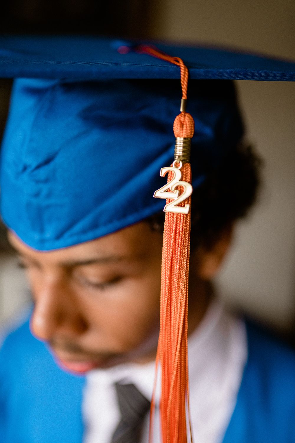 Close-up of graduation cap with orange 2022 tassel against blue background.