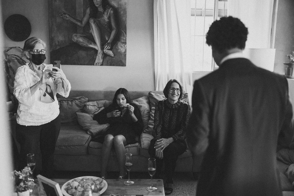 Black and white photo of friends gathering in living room with photographer.