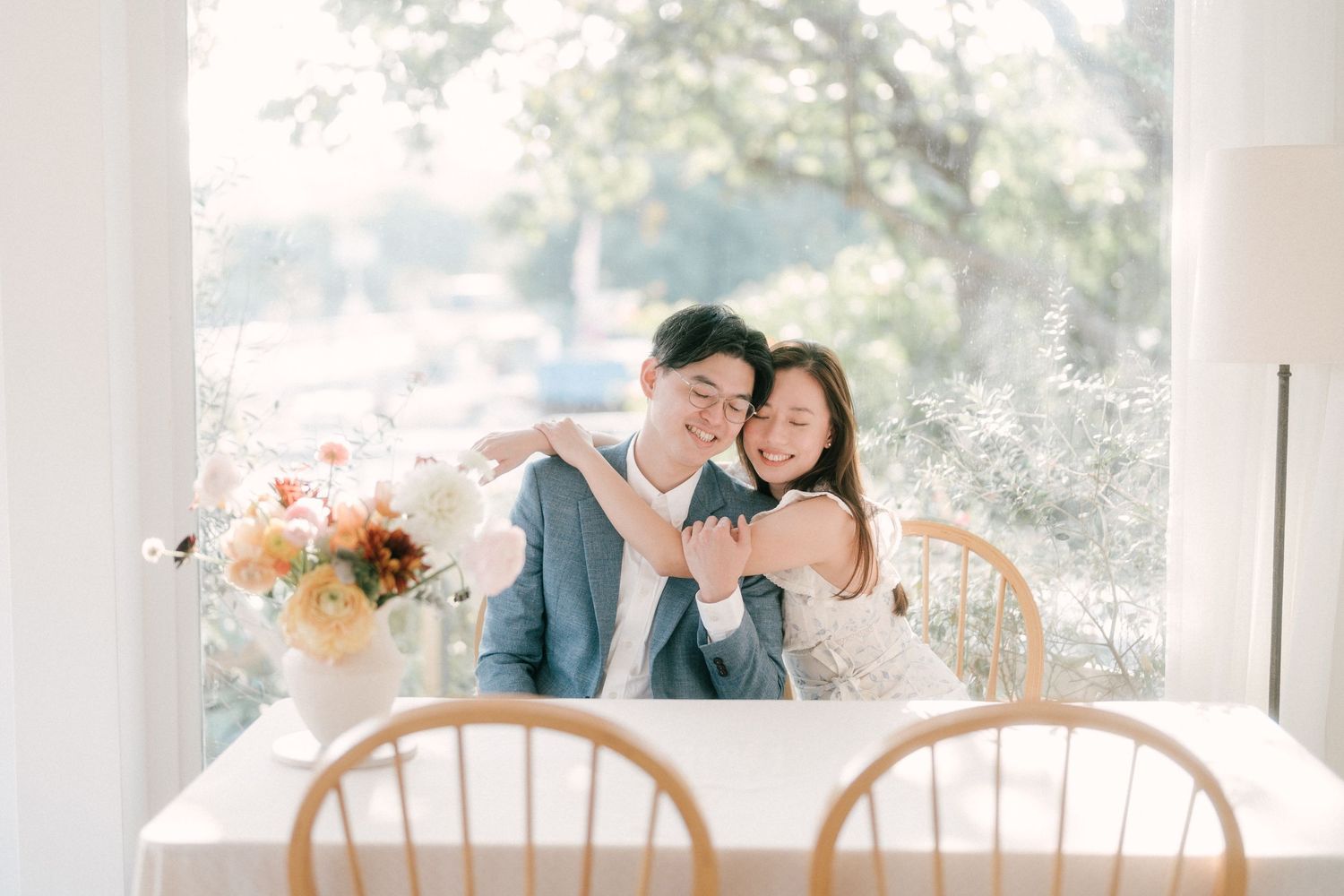 Joyful couple sharing an intimate moment at a bright indoor dining setting with floral arrangements.