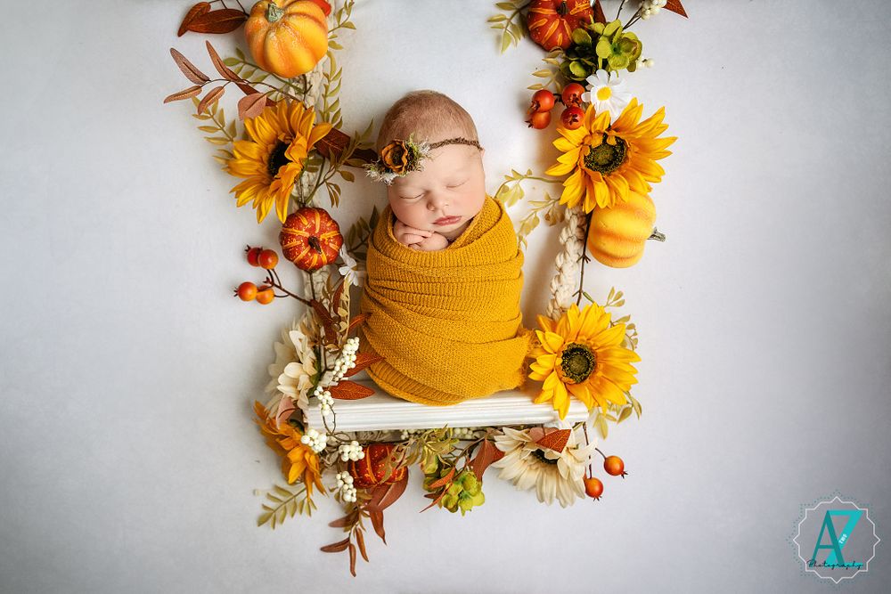 Newborn wrapped in mustard yellow blanket surrounded by fall flowers and sunflowers.