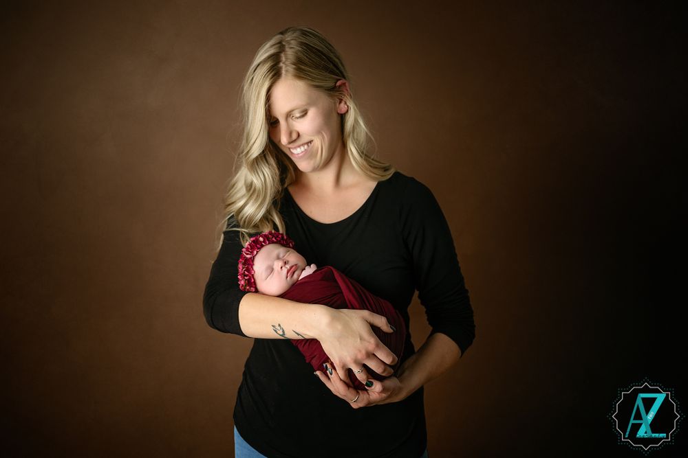 A tender newborn photography session features a parent in black cradling a baby wrapped in burgundy fabric.
