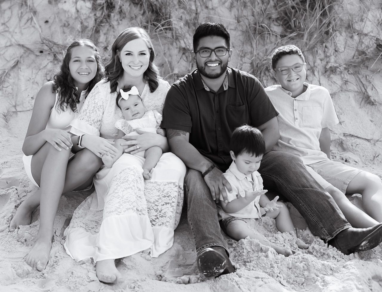 Black and white family portrait on a beach with a small dog.