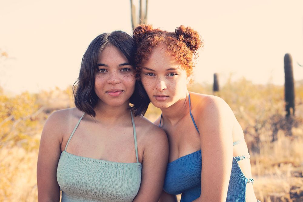 Two people in sundresses pose together against a desert landscape at golden hour.
