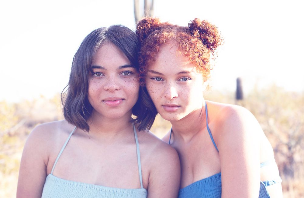 Close portrait of two people in sundresses with desert scenery behind them.