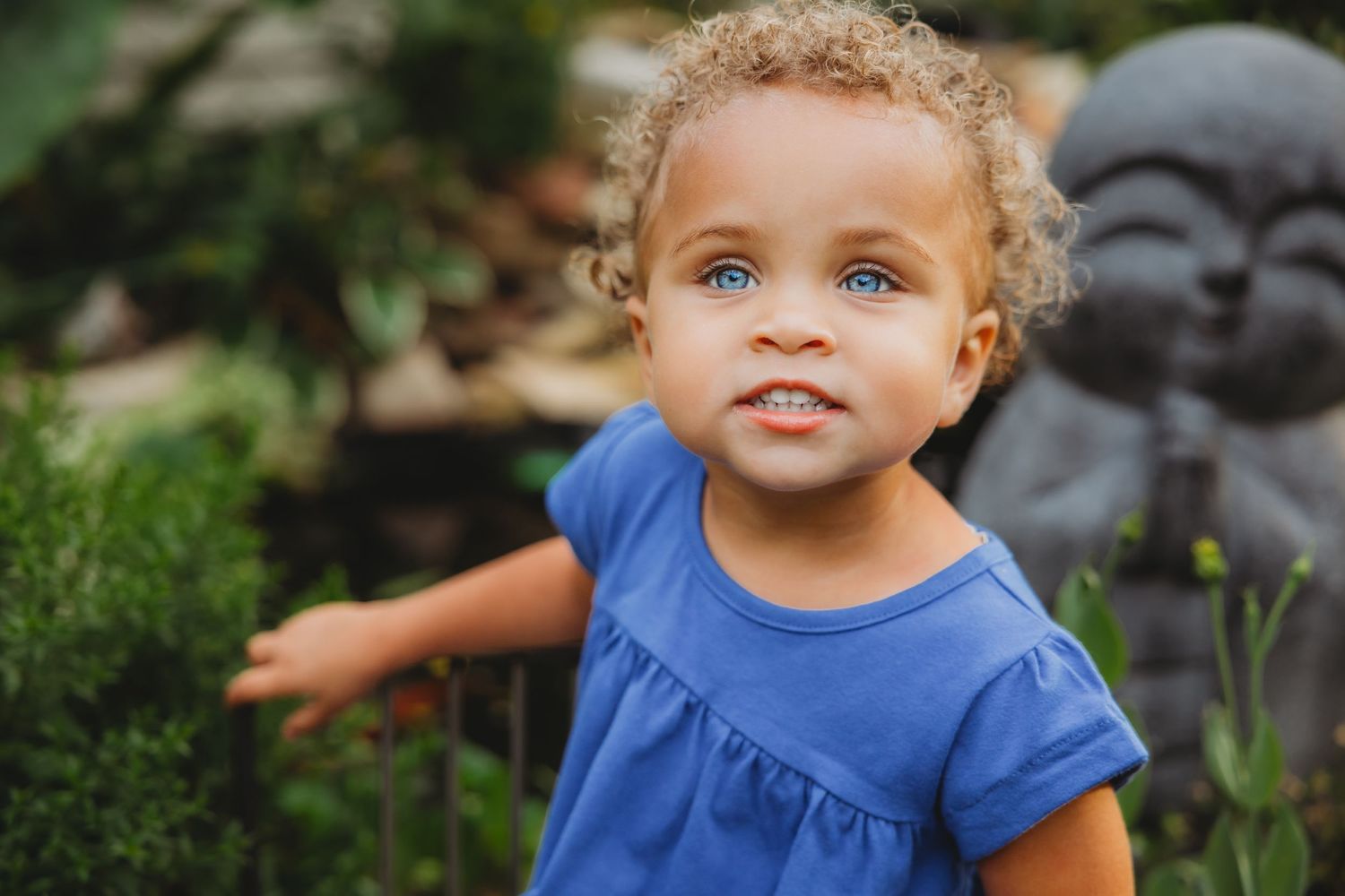 Close-up portrait of a child with bright blue eyes wearing a blue shirt outdoors.