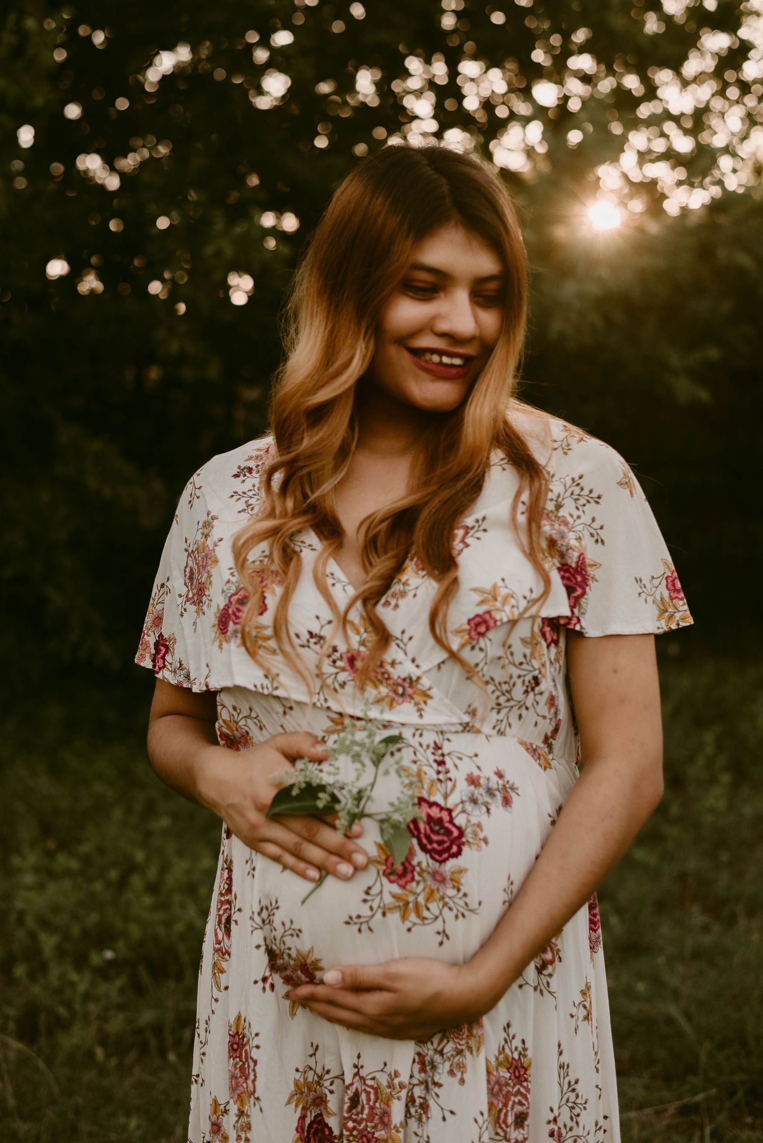 Beautiful maternity portrait at sunset with floral dress in natural outdoor setting.