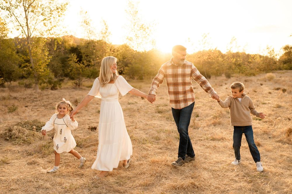 Santa Barbara golden grassy field family photos by Ventura family photographer of family walking holding hands in sunlight during photoshoot