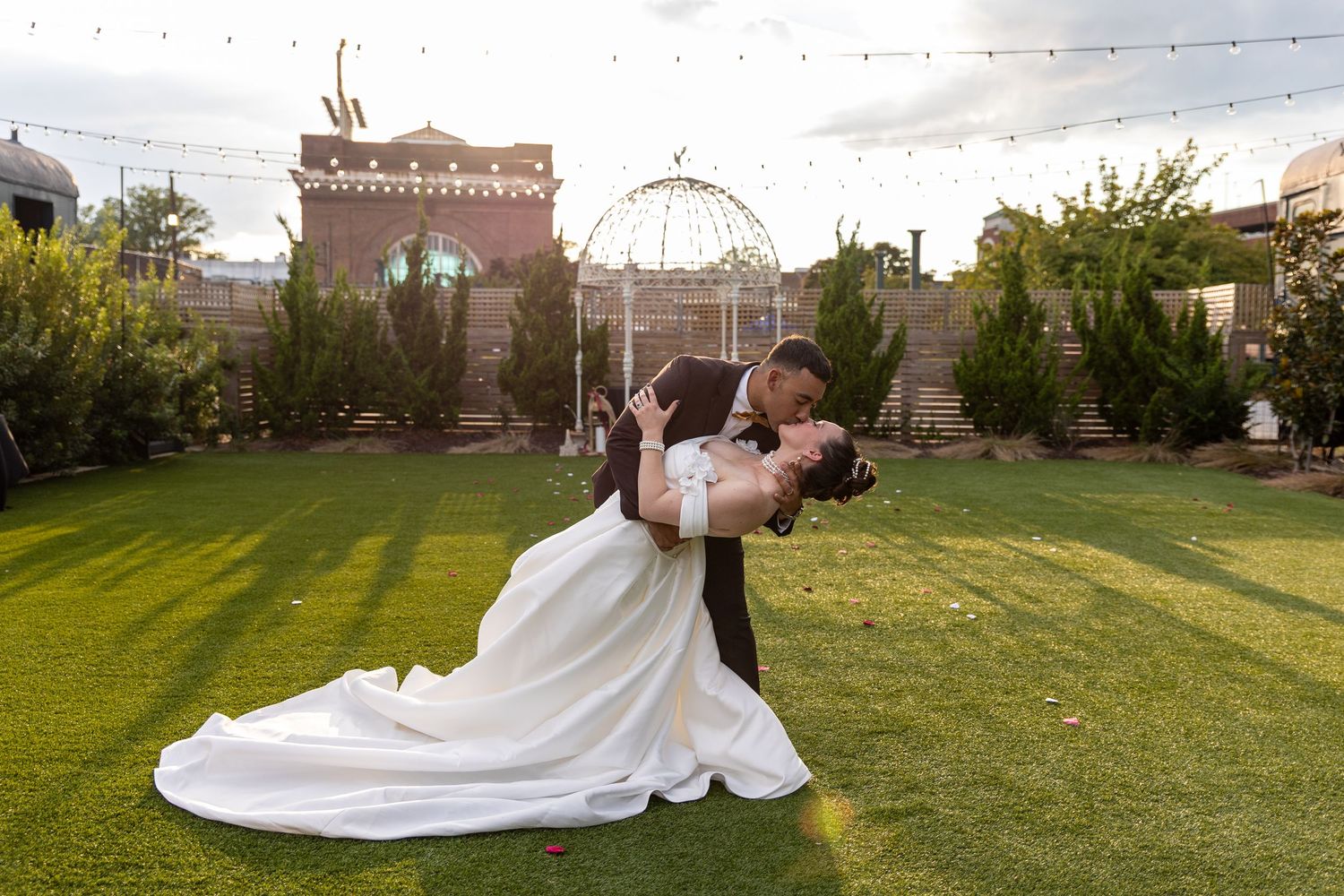 A groom dips his bride dramatically on a green lawn at an outdoor wedding venue.