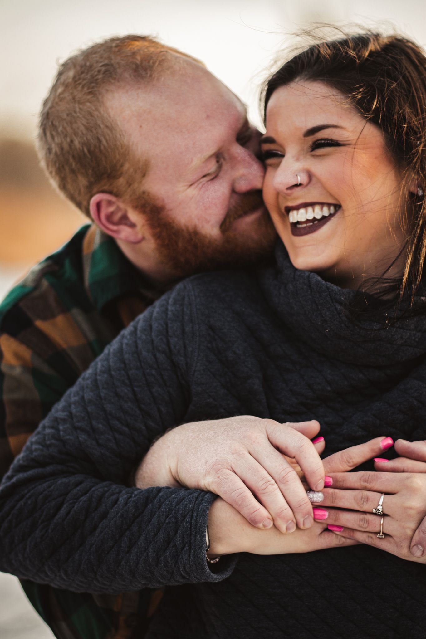 A couple shares a candid laughing moment while showing off an engagement ring.