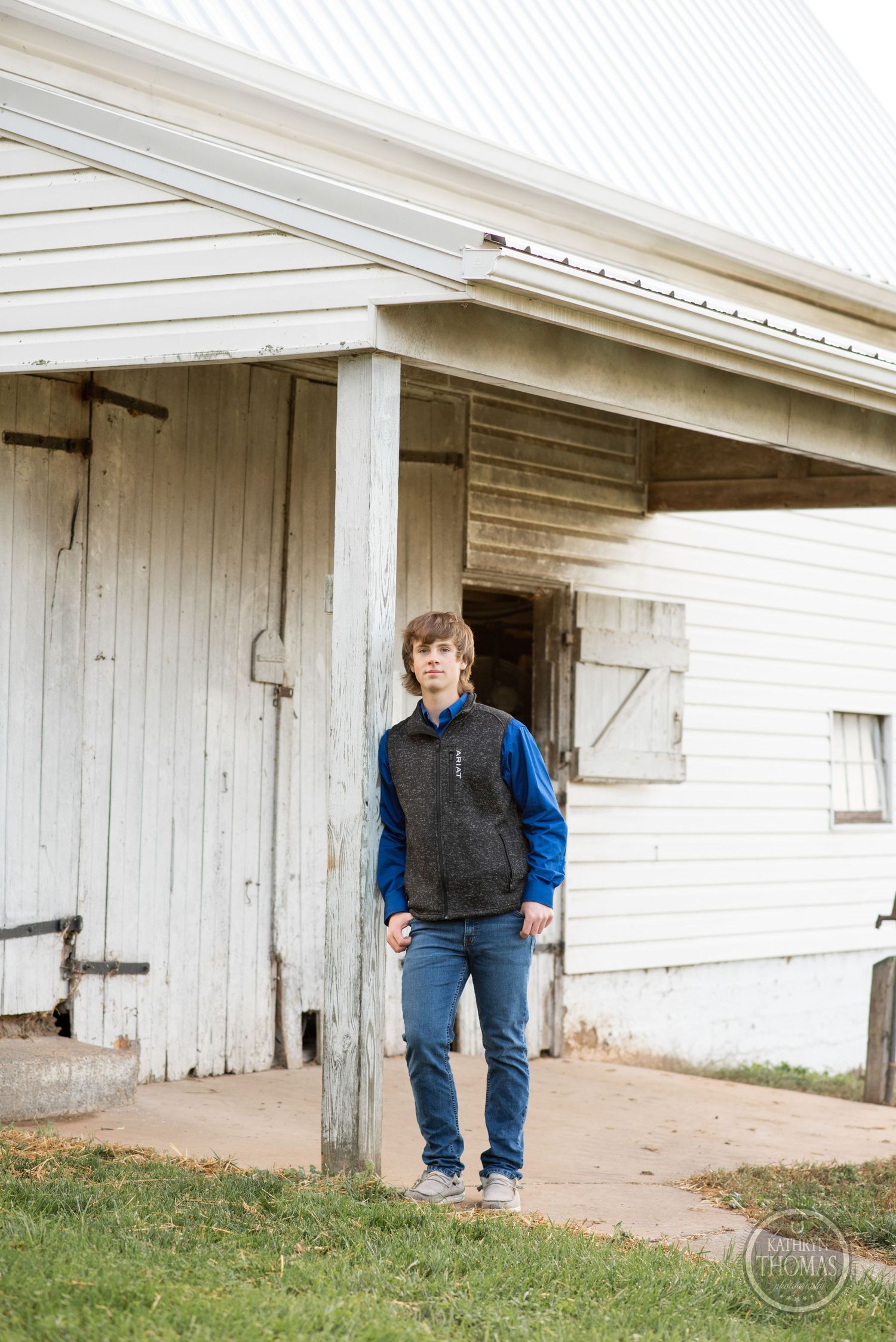 Person in casual outdoor wear stands in front of weathered white barn entrance.
