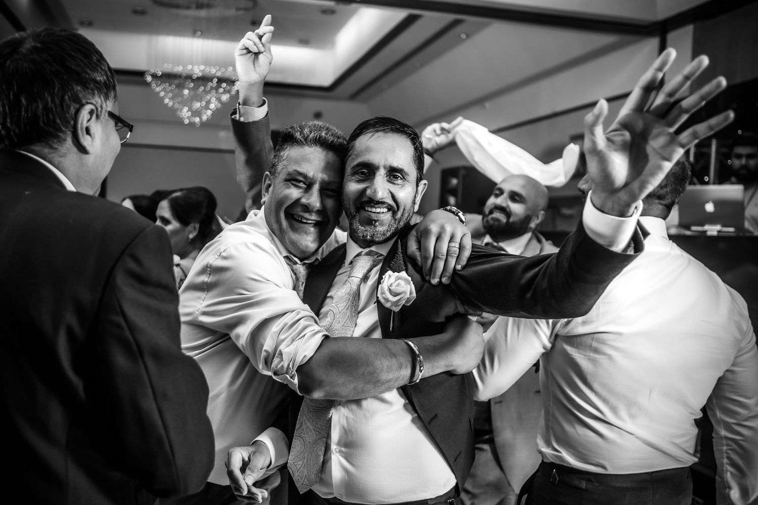 Black and white photo of groomsmen celebrating with joyful embraces at wedding reception.