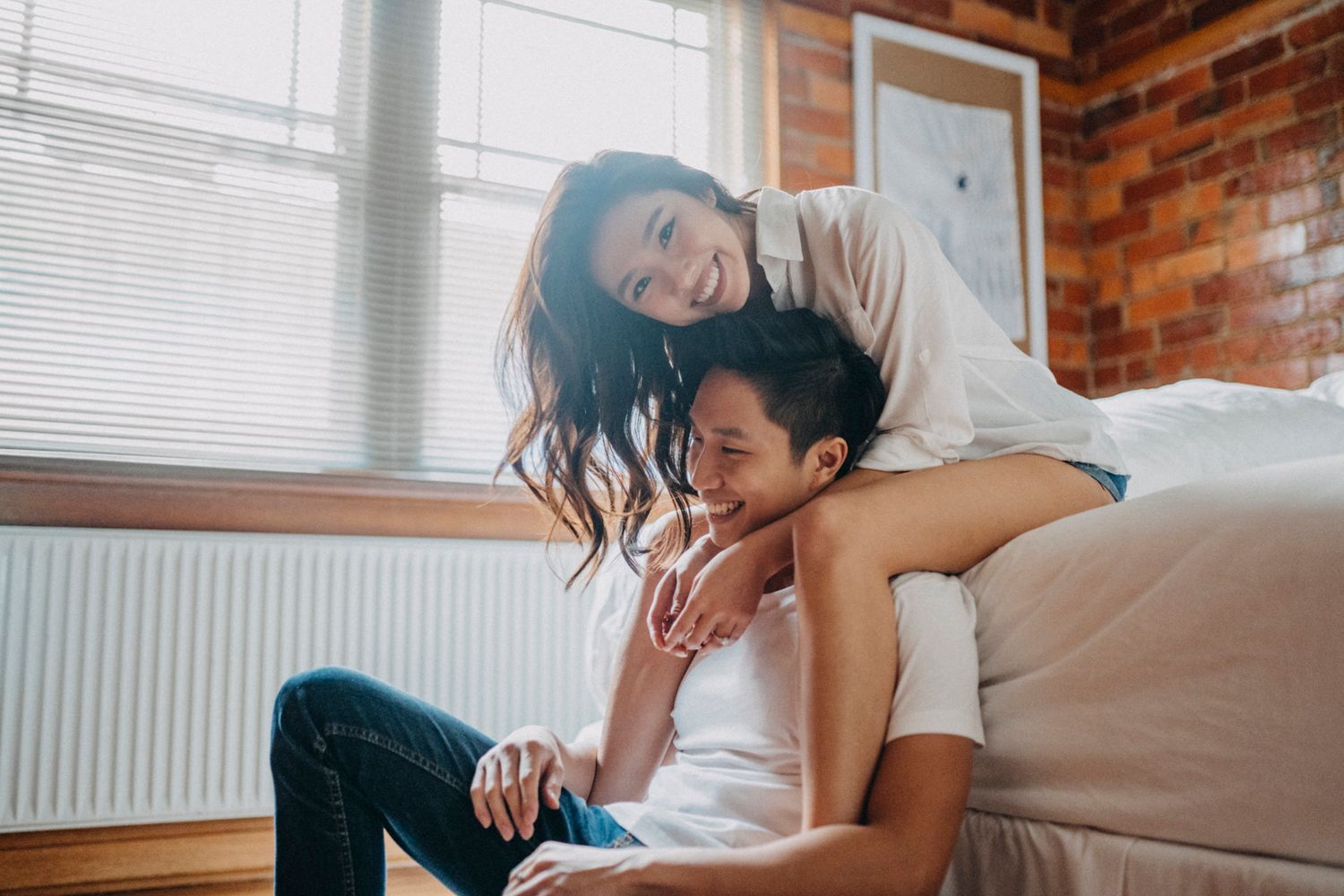 Intimate couple shares tender moments in rustic brick-walled room with natural lighting.