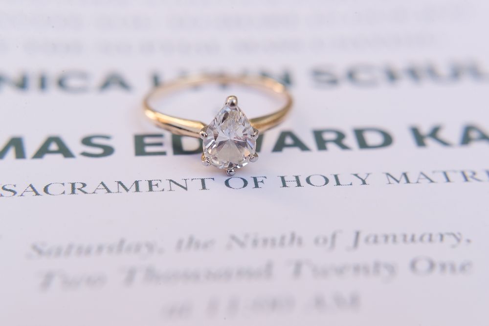 Delicate pear-shaped engagement ring displayed on wedding invitation.