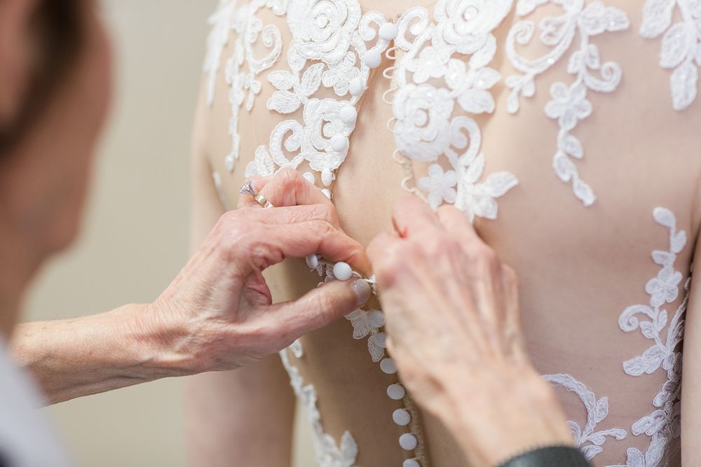 Close up of delicate lace details being adjusted on a white wedding dress.