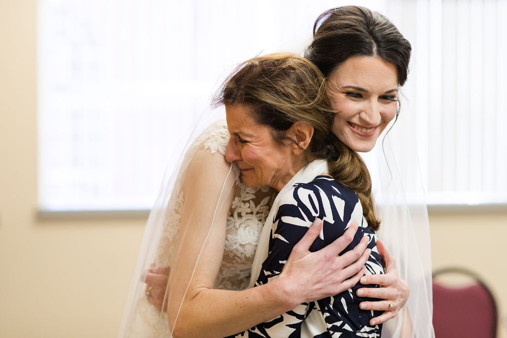 An emotional embrace during wedding preparations in a sunlit room.