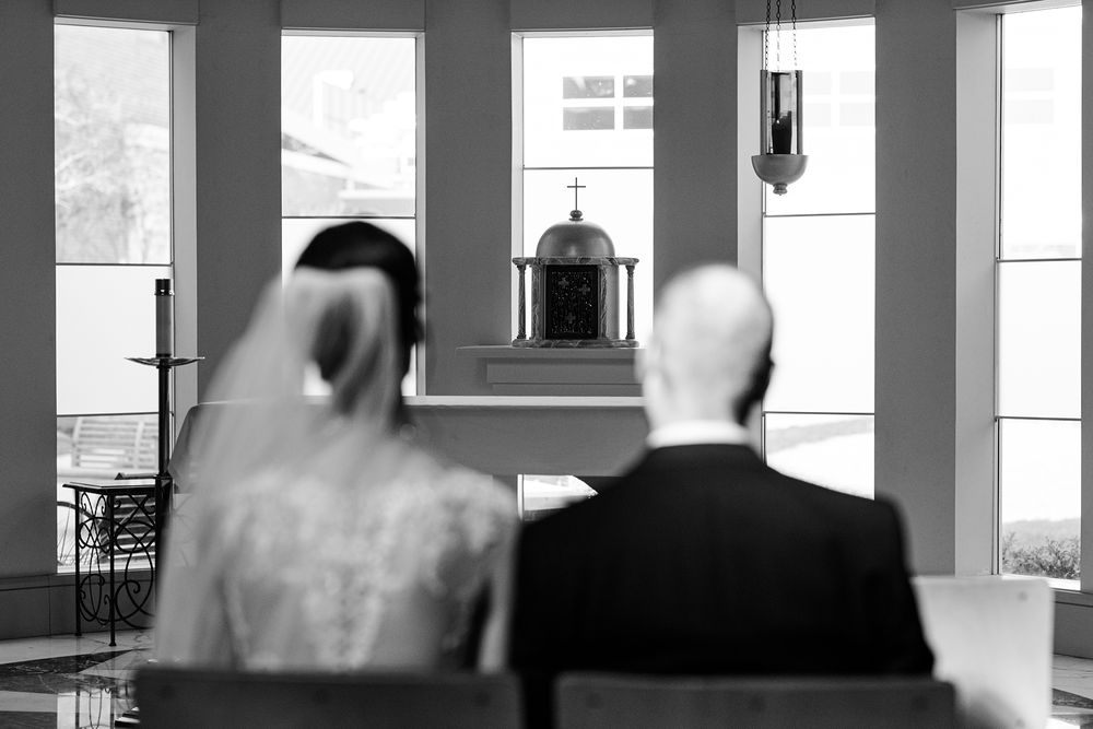 Black and white view of wedding ceremony from behind in bright windowed room.