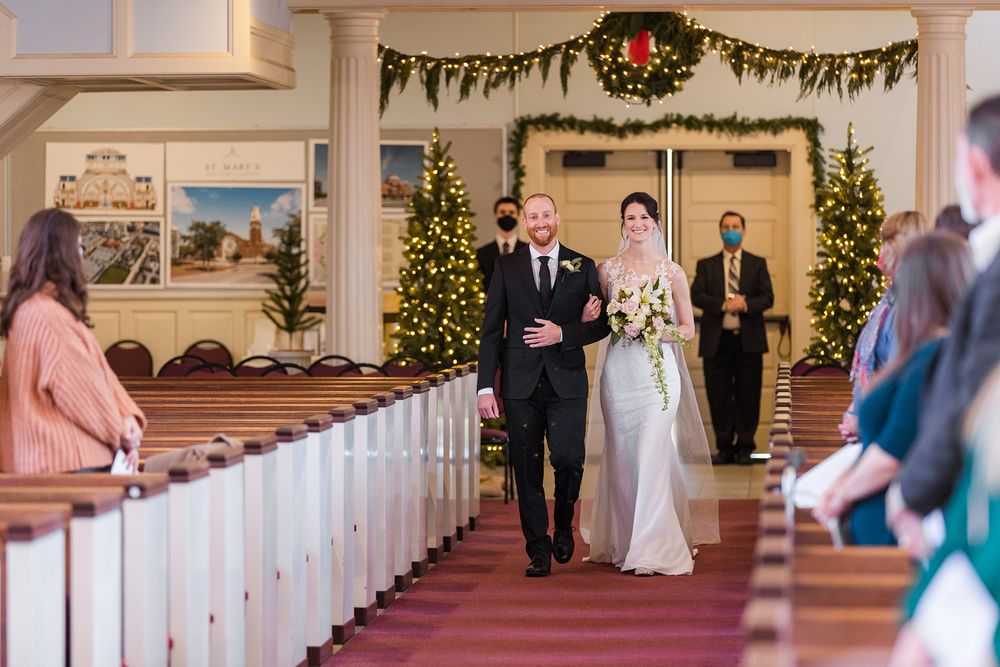 Wedding ceremony processional in church decorated with Christmas trees and garland.
