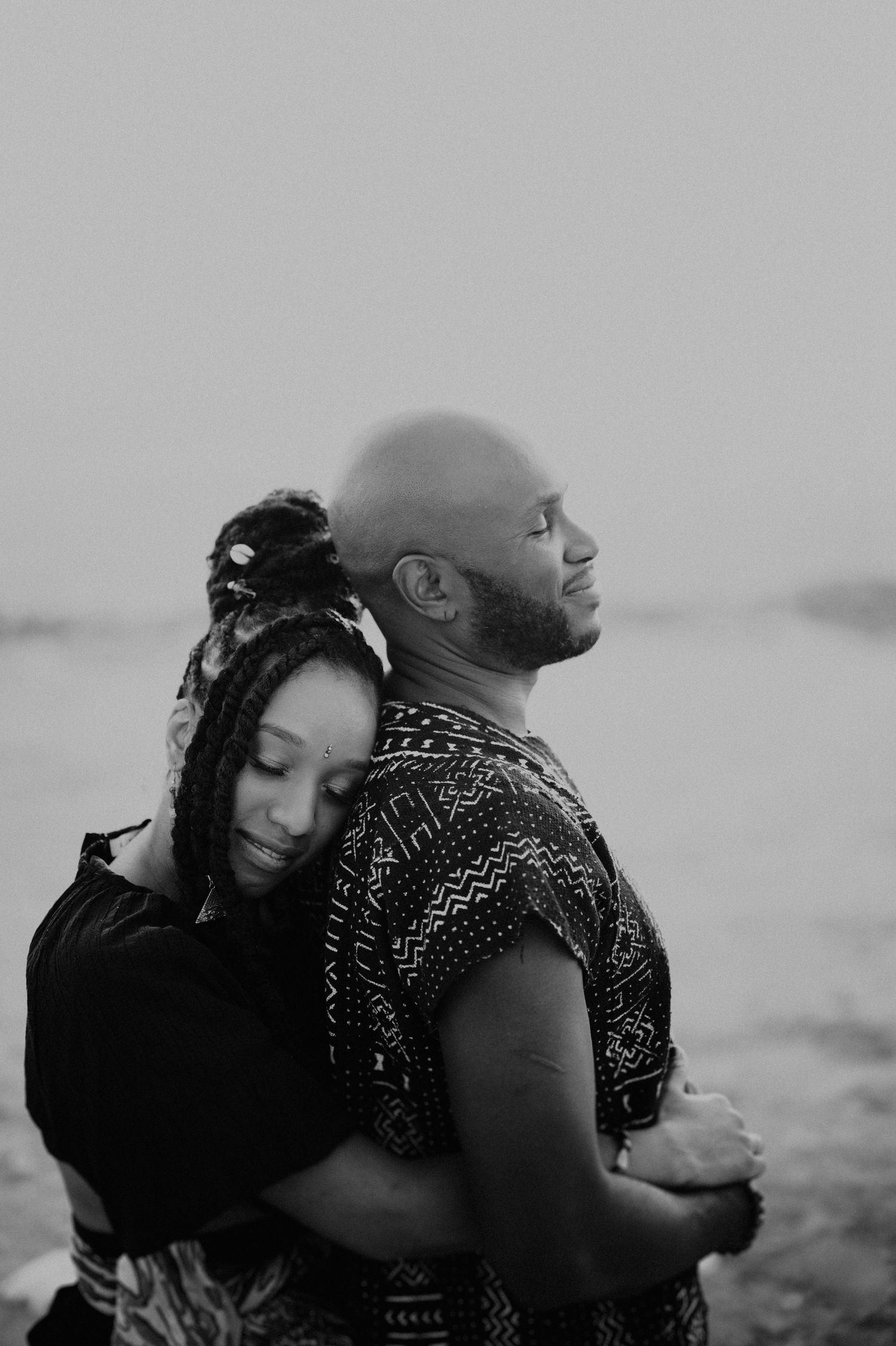 An intimate black and white portrait of a couple embracing on a misty beach.