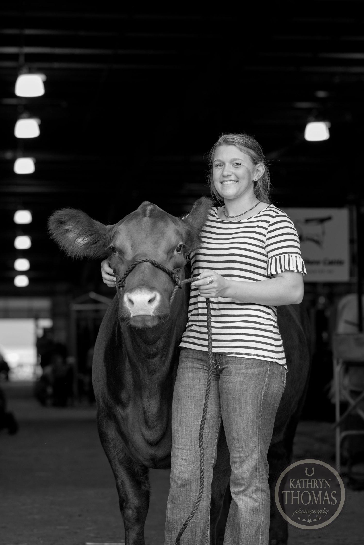 A black and white portrait of a person with their show cow under barn lighting.