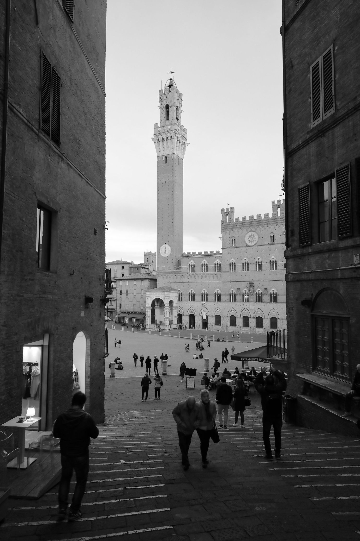 Black and white view of Siena's Palazzo Pubblico and Torre del Mangia with pedestrians in the square.