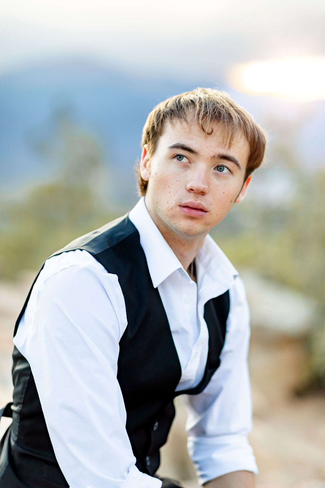 Senior guy sits on a rock and gazes to the side at sunset at his senior session at Palmer Park in Colorado Springs.