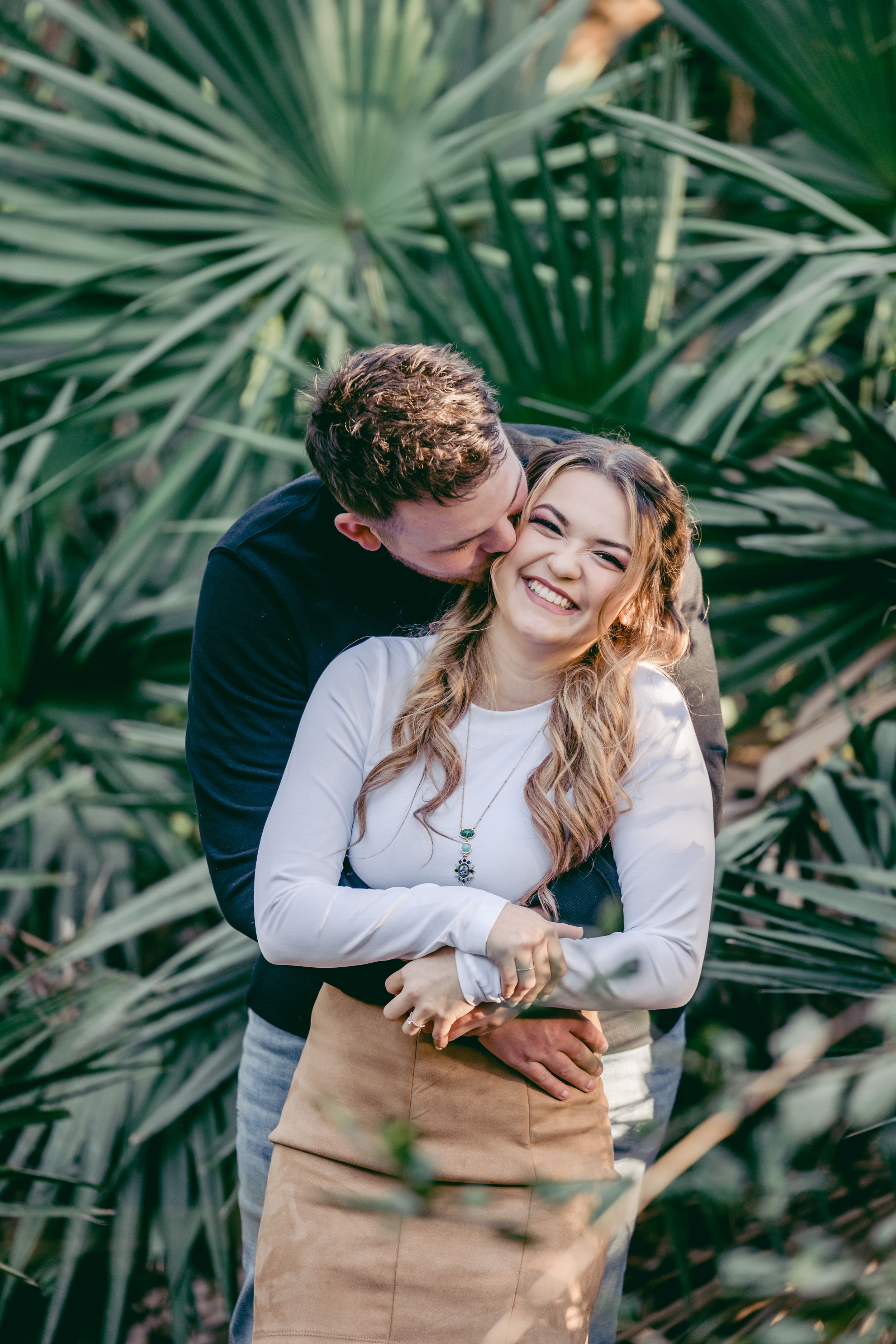 A joyful engagement session with palm fronds creating a tropical backdrop.