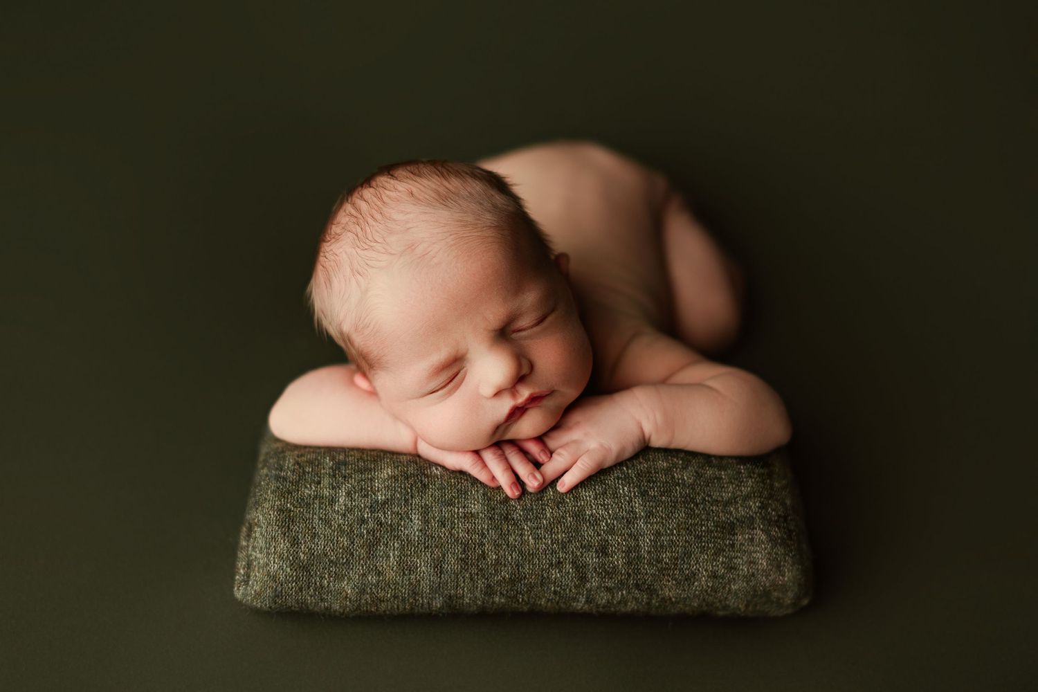 Peaceful newborn sleeping on olive green cushion with crossed arms.