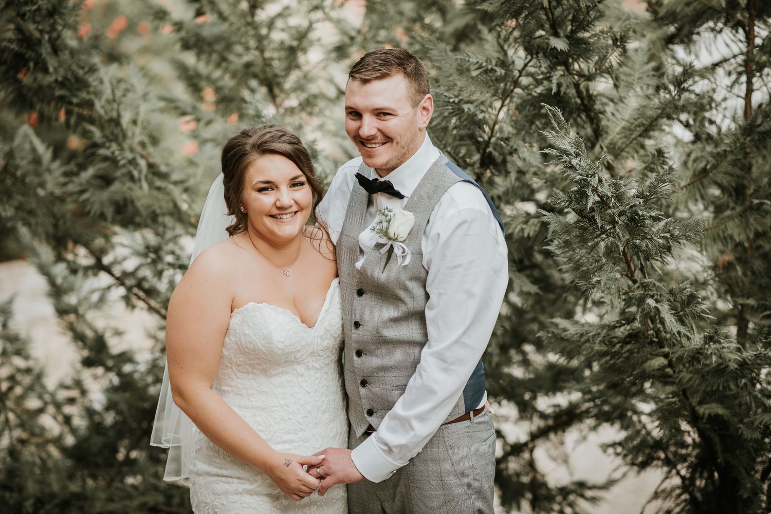 Wedding couple shares intimate moment surrounded by lush greenery and trees.