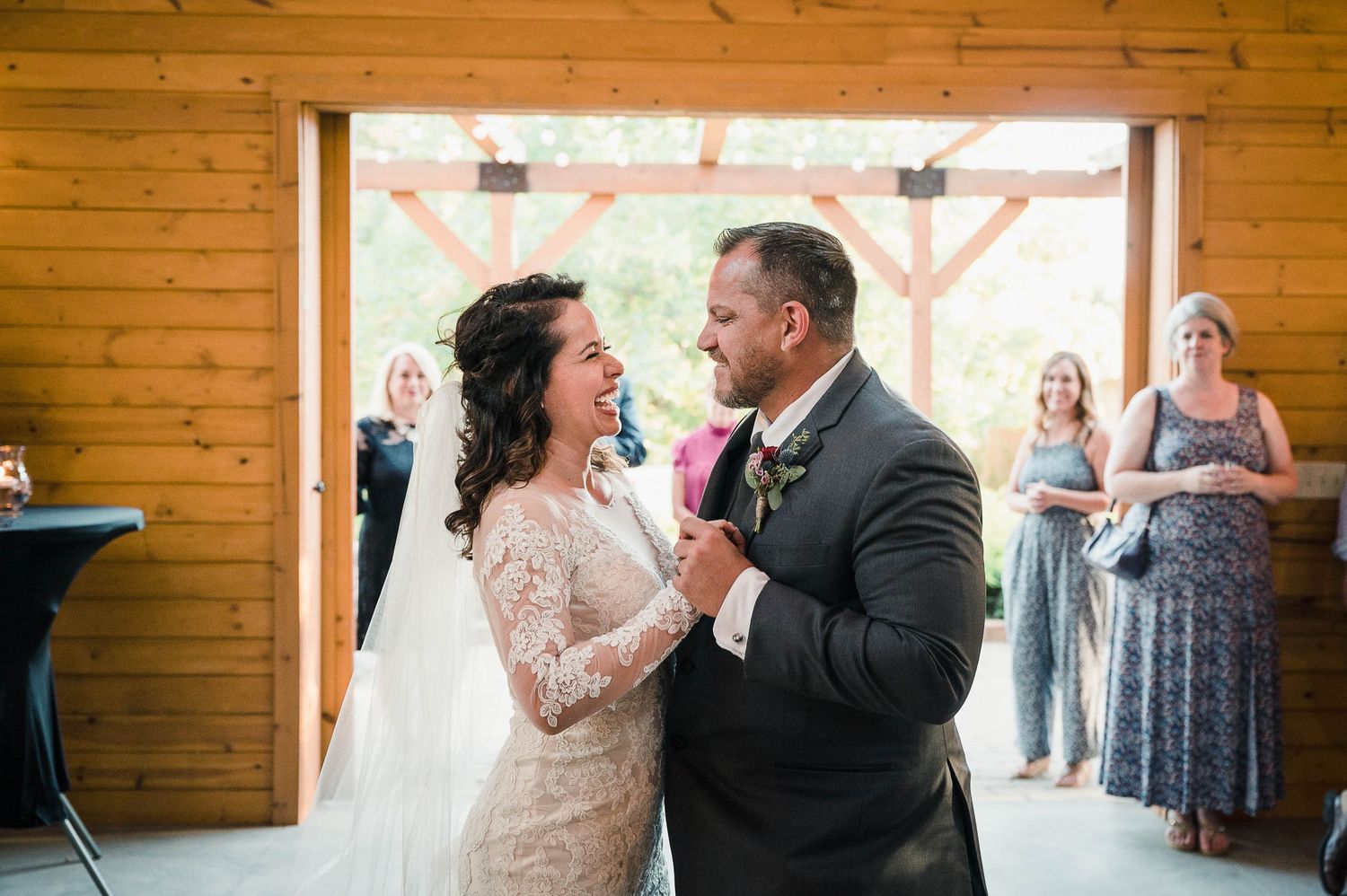 Romantic first dance moment in rustic barn wedding venue with string lights overhead.