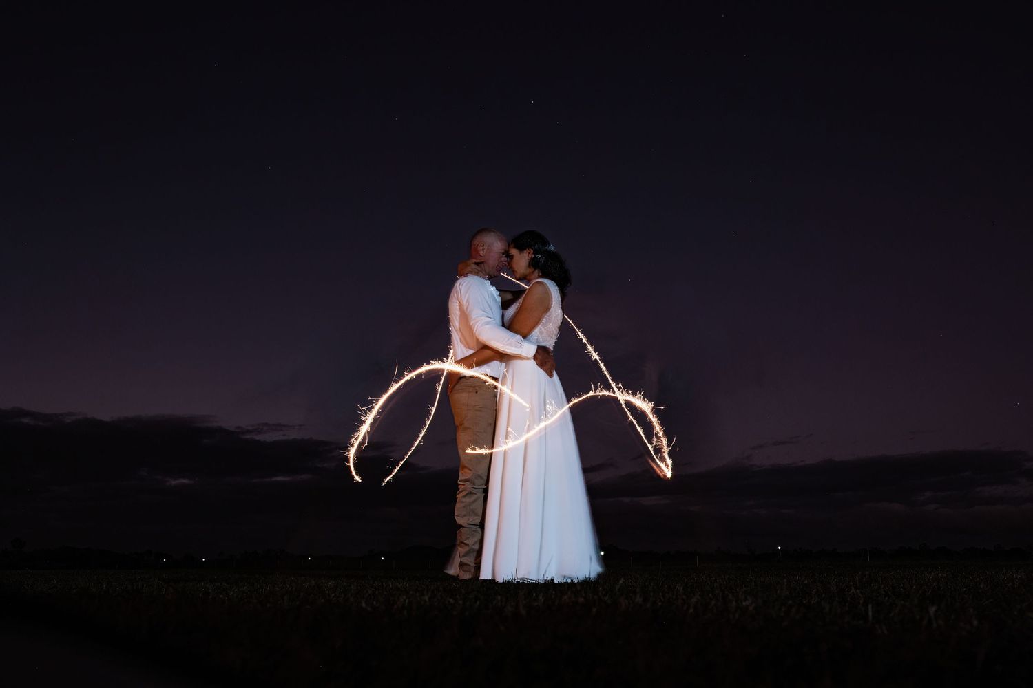 Couple creates romantic light painting with sparklers against dark night sky backdrop.