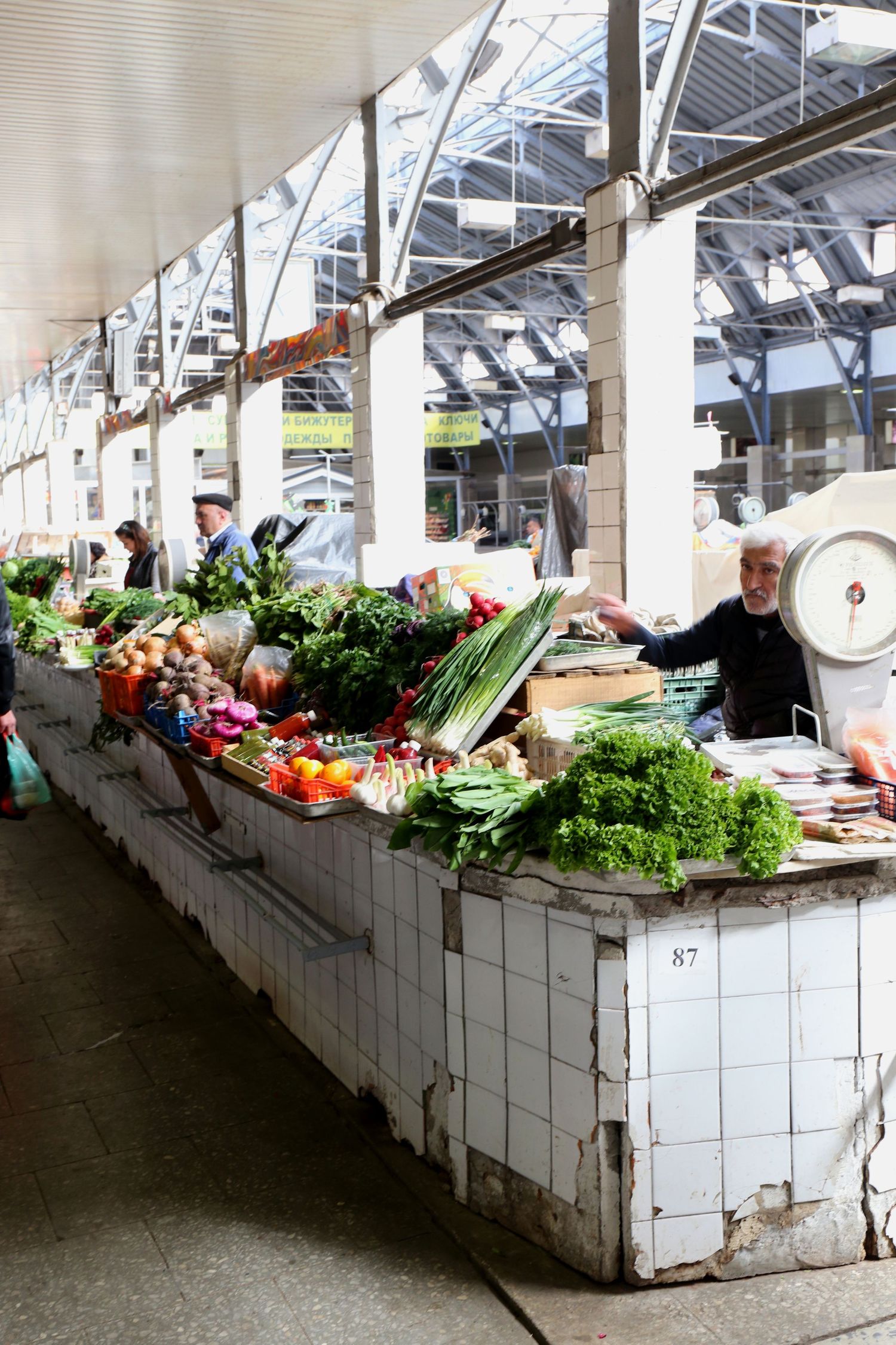 Fresh produce and vegetables displayed at a traditional market stall with white tiled counters and steel roof structure.