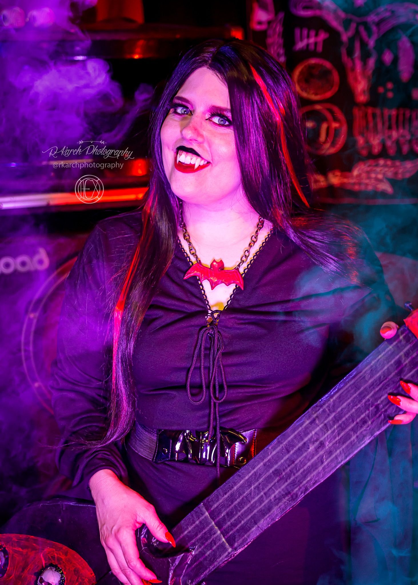 Bass player in Gothic attire performs under dramatic purple lighting at rock concert.