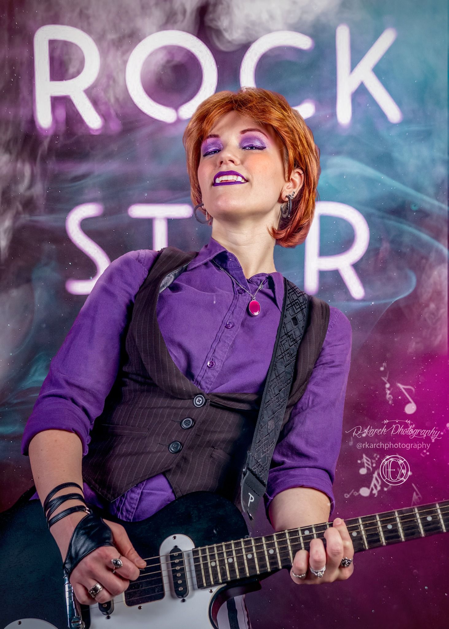 Guitarist in purple shirt and black vest performs energetically under neon rock star sign.