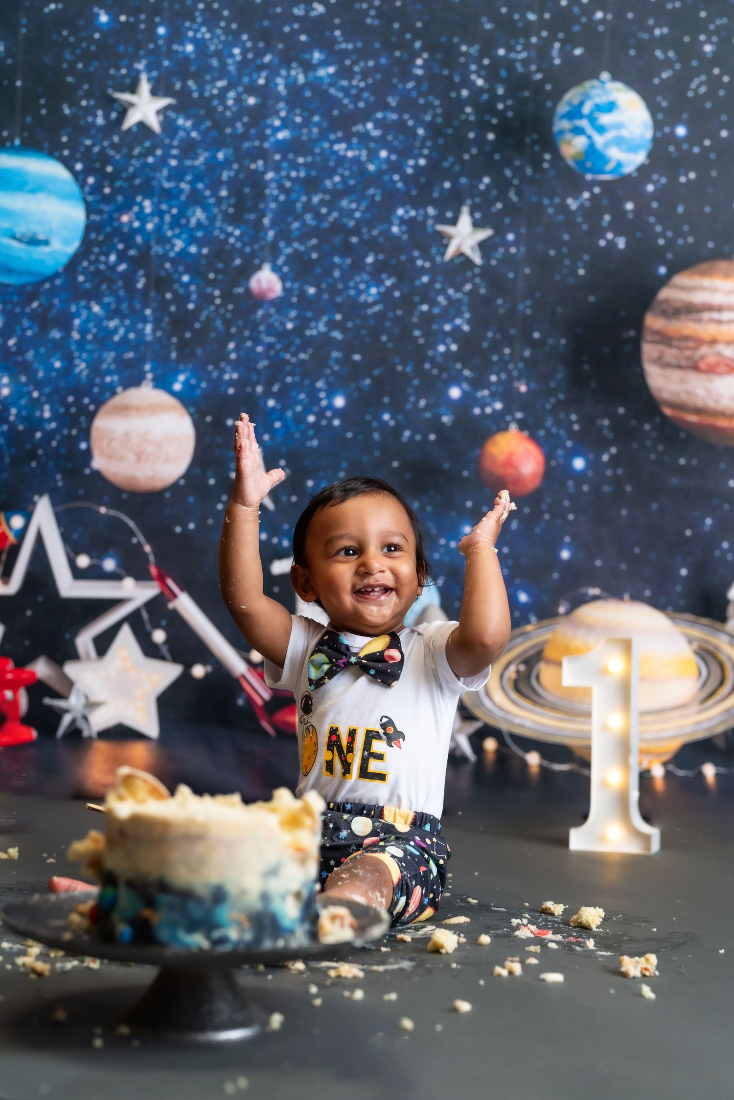 Space-themed first birthday cake smash with planets and stars backdrop.