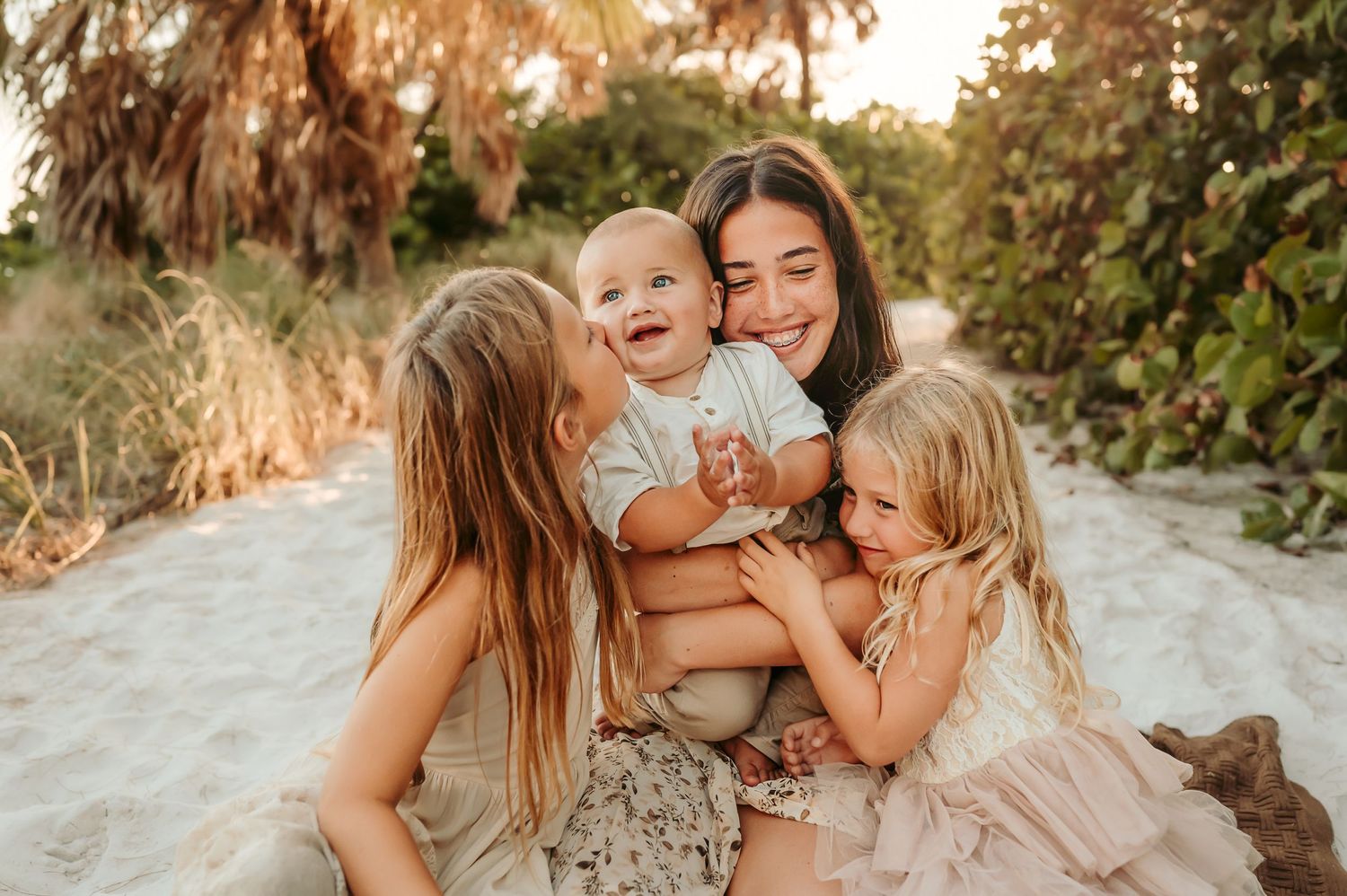 Family of kids embrace in one big hug while sitting on the sand at the beach.