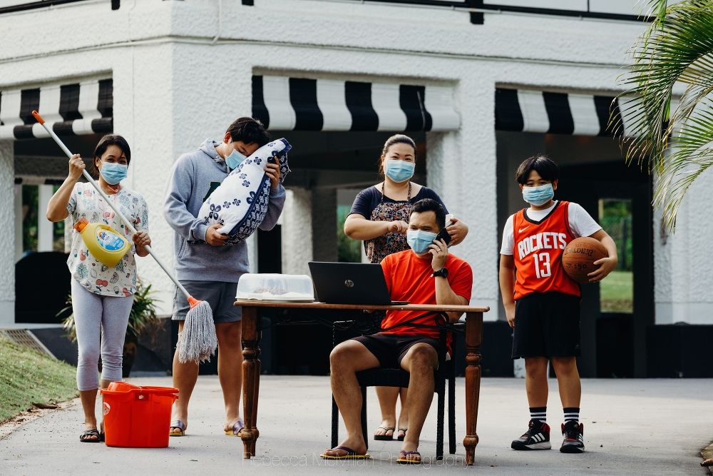 A family holds individual items to represent their pandemic experience, outside their house