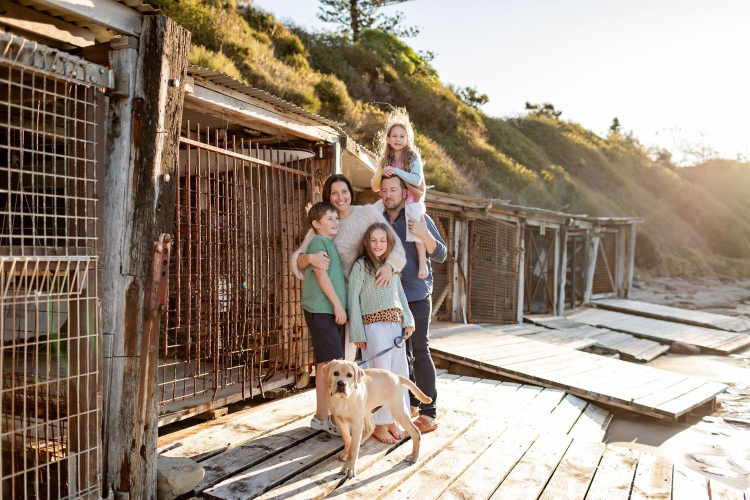 Family and dog posing together on wooden deck during sunset at coastal location.