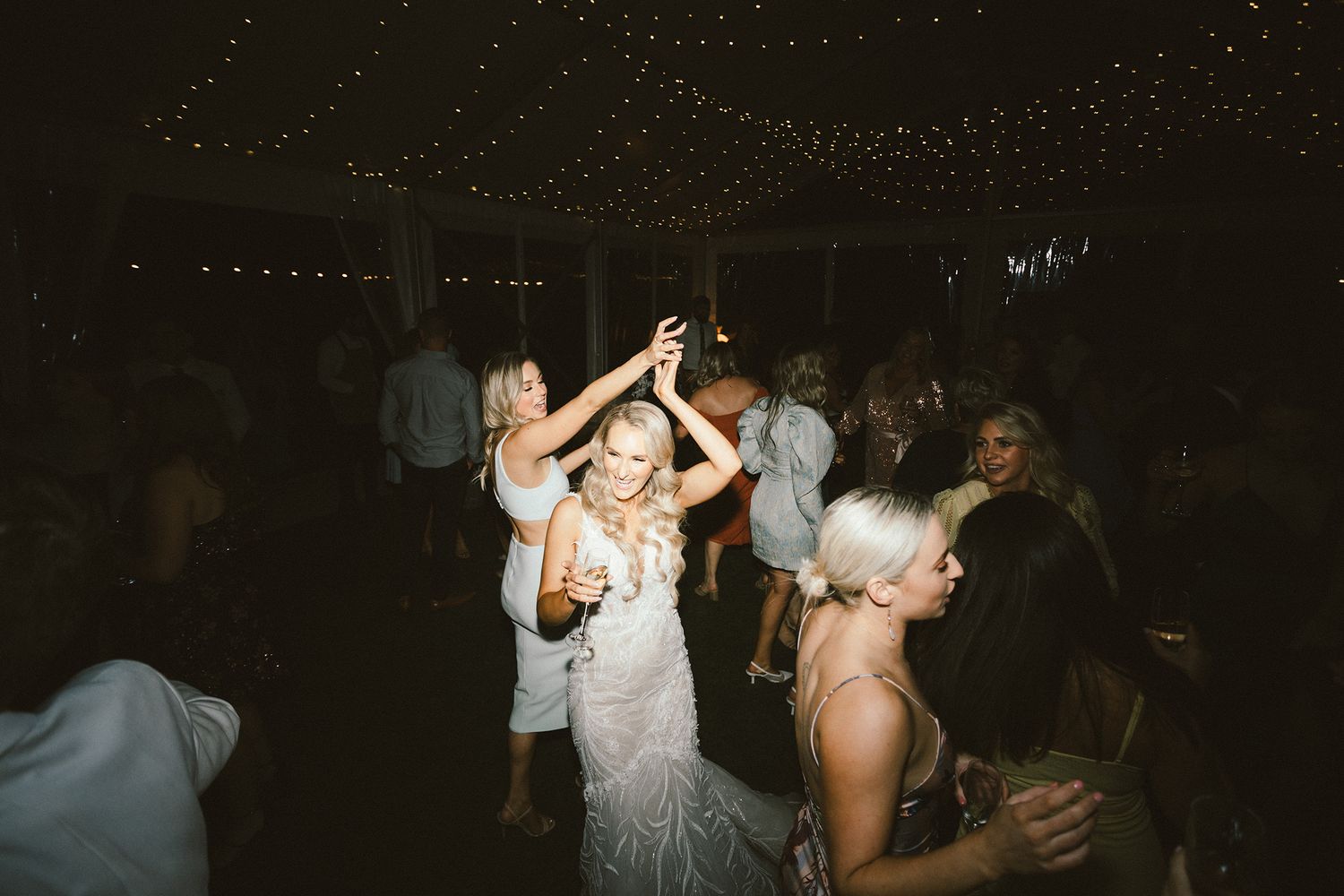 Lively reception dance floor with partygoers celebrating under dimly lit string lights.