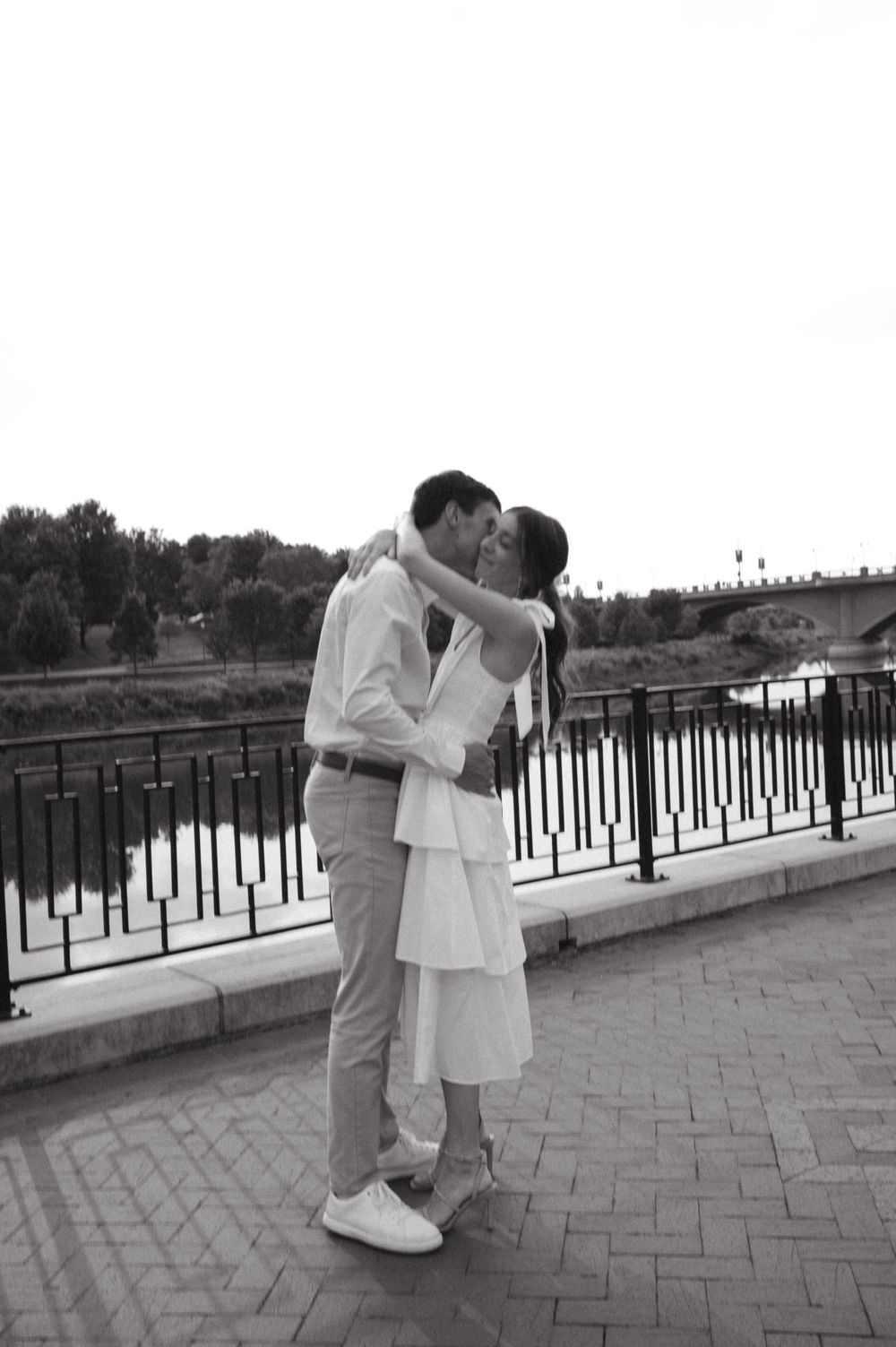 A black and white photo captures a tender moment between a couple on an urban bridge.