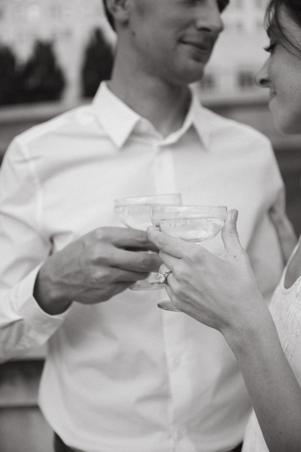 A couple in formal attire shares a toast with champagne glasses in black and white.