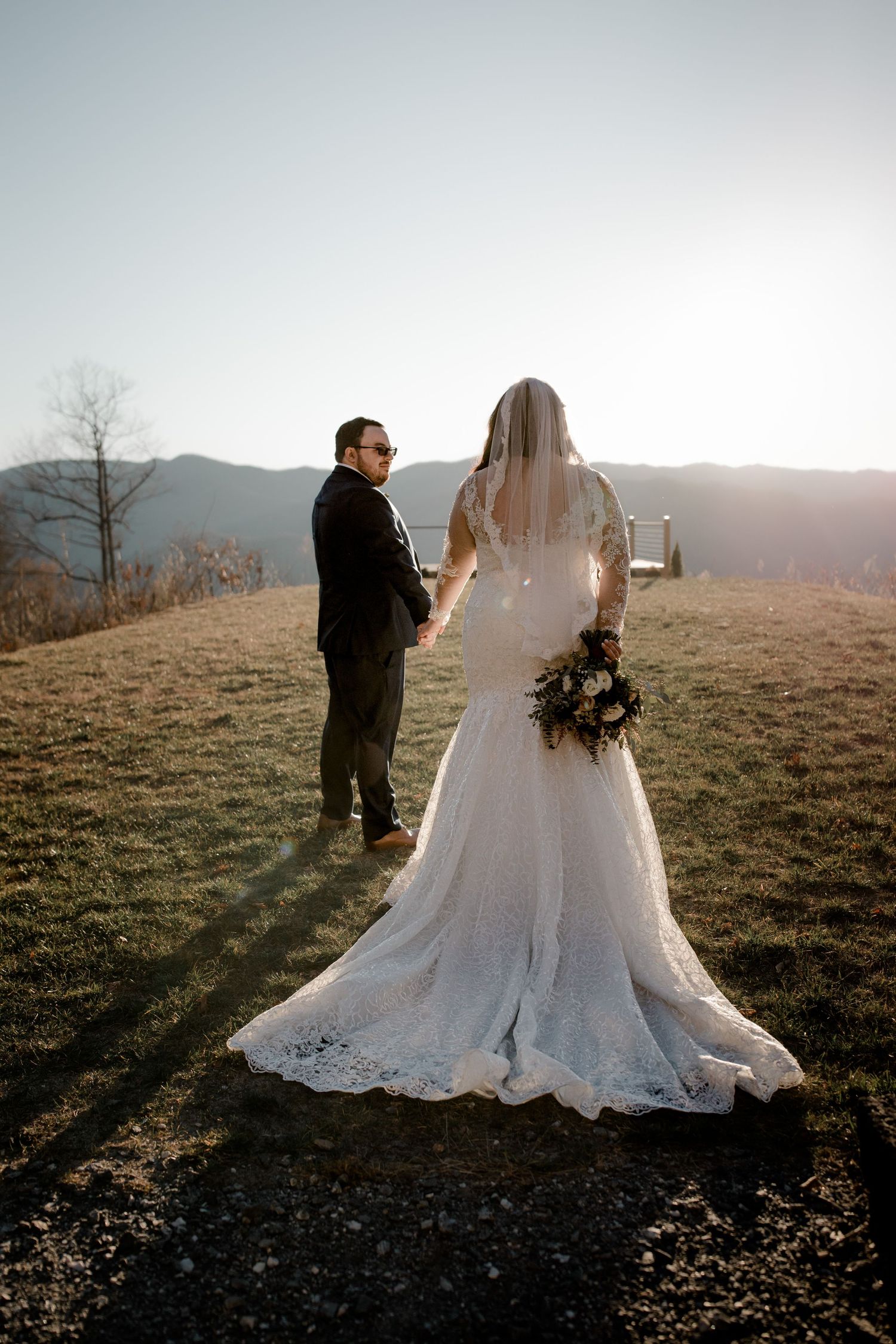 Wedding couple standing on mountain overlook during sunset in full wedding attire.