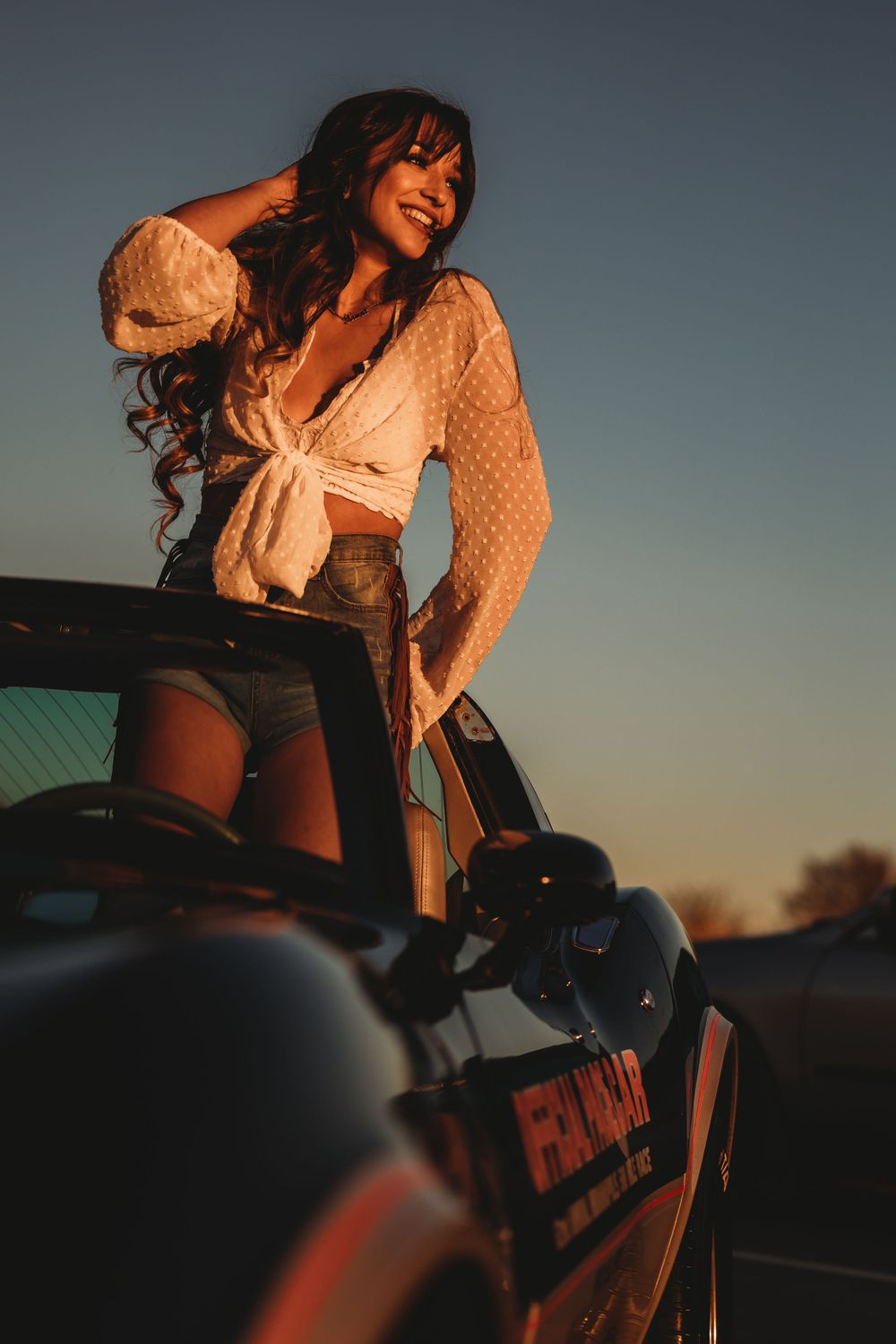 Woman in white lace top posing on a motorcycle during sunset.