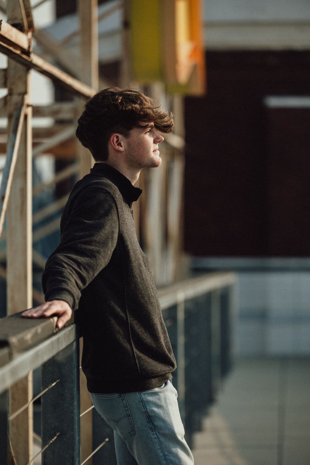 Side profile portrait at railing with industrial background.