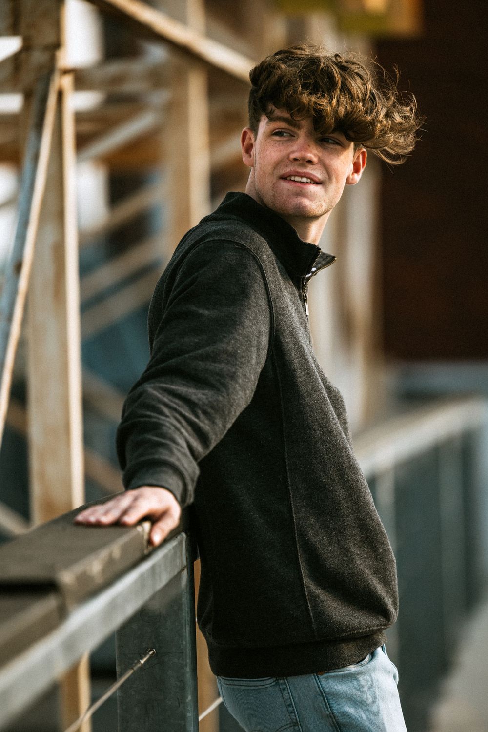 Casual portrait leaning on metal railing in black jacket and jeans.