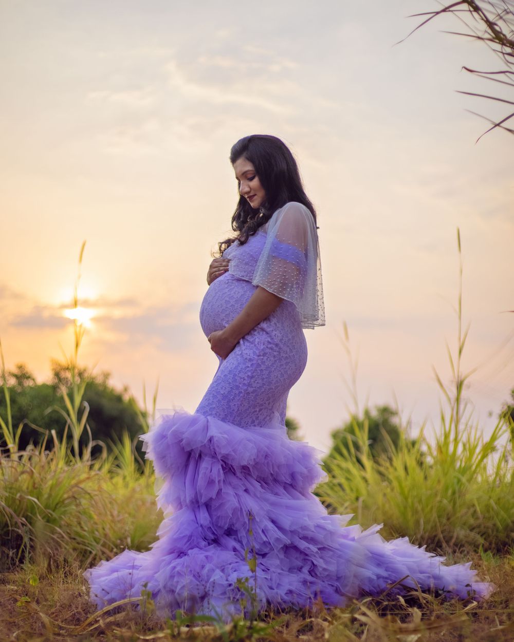 Maternity portrait in a purple tulle dress during sunset with tall grass in the background.