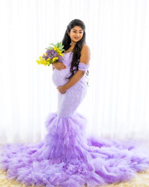 Maternity photo with lavender mermaid dress and colorful bouquet against white backdrop.