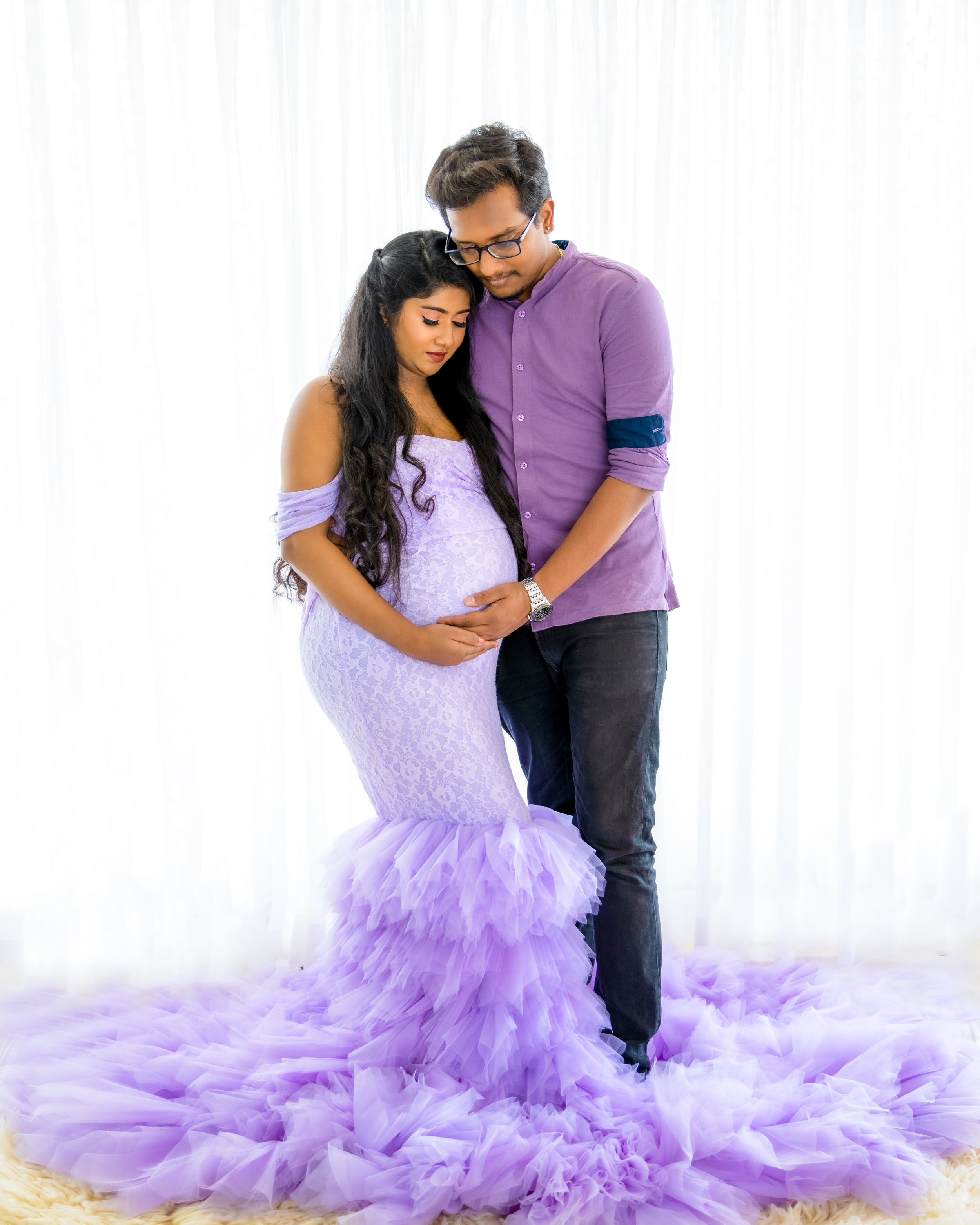 Intimate maternity portrait with couple in purple and lavender tones against white background.
